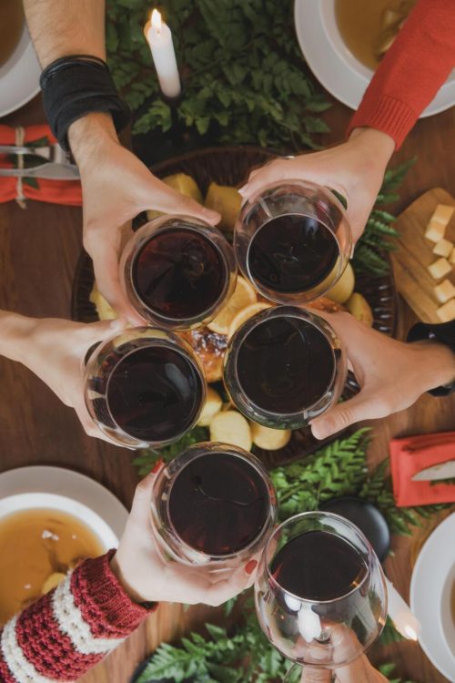 hands holding red wine in glasses clinking them together for a cheers.